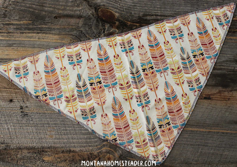 How to make a simple dog bandana easy DIY tie on dog bandana feather print colorful fabric dog bandana finished and laying on rustic piece of barn wood