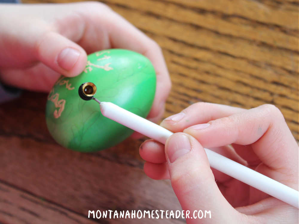 How to make Pysanky eggs decorate blown eggs using a Kistka tool to draw designs with wax on the egg then dye the egg using wax resist methods child using a Kistka tool to draw on green egg with wax